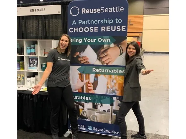 Two people stand on either side of a Reuse Seattle sign