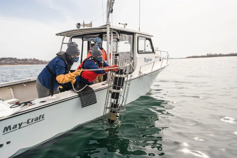 Two scientiests on a boat lower instrument into the waters of a seaweed farm off the coast of Maine
