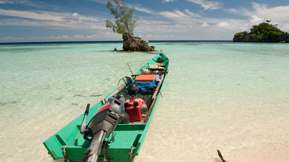A long and thin fishing boat floats in shallow, clear water in Indonesia.