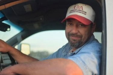 A man in a baseball hat looks out the window of a pickup truck