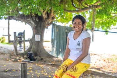 A woman in a yellow skirt sits and smiles at camera