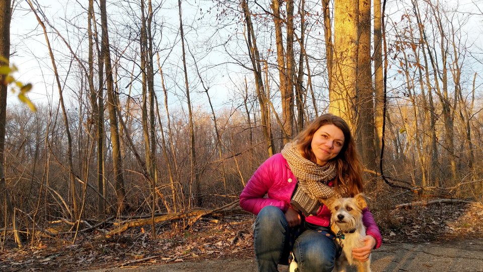 A women poses with her dog in the woods