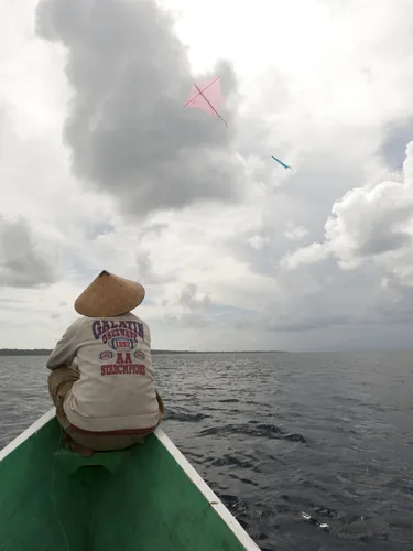 A person sits facing forward on the front of a narrow boat, looking out at the ocean ahead