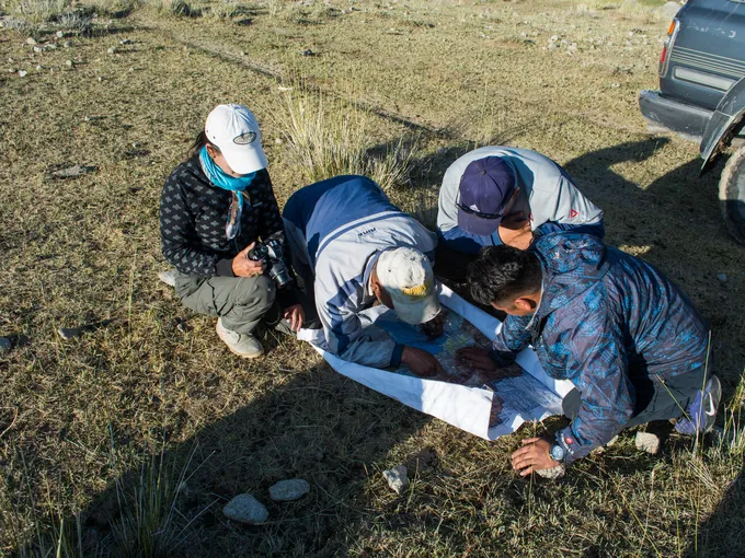 A team of surveyors look at a paper on the ground as they count snow leopards in Mongolia