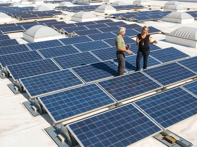 Two people standing among rooftop solar panels.