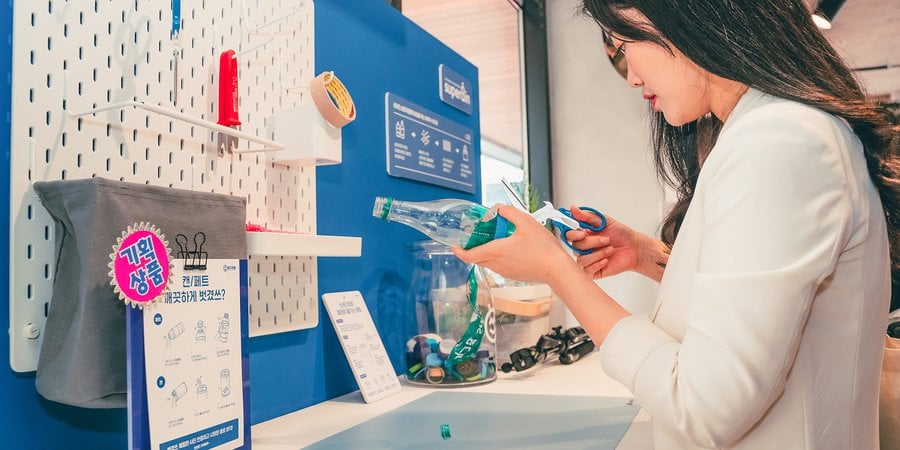 A woman with long black hair cuts up a plastic bottle to recycle it.