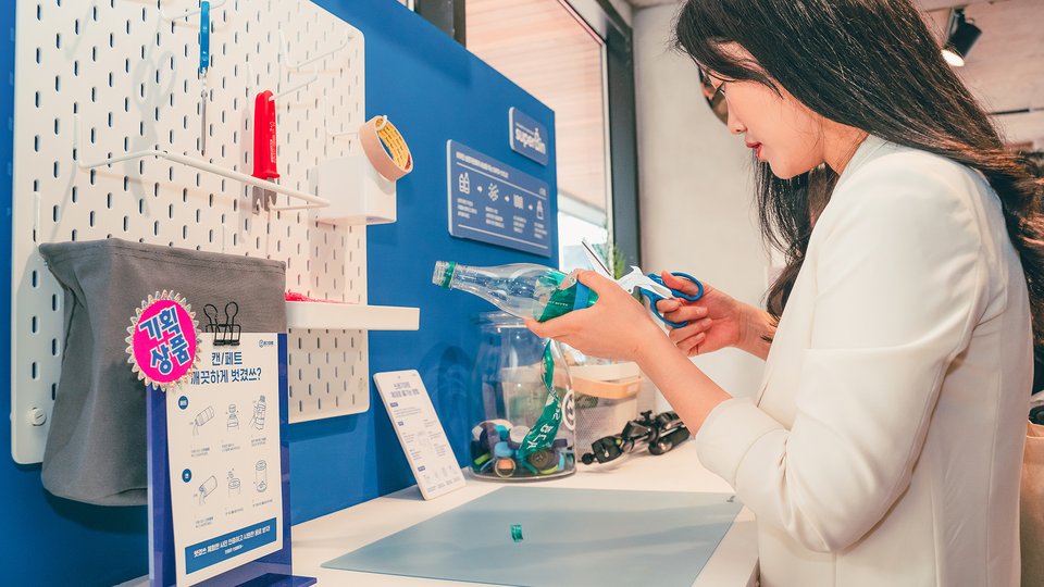 A woman with long black hair cuts up a plastic bottle to recycle it.
