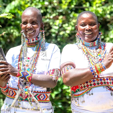 Two smiling women in colorful African dress hold up potted plantss