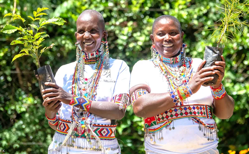 Two smiling women in colorful African dress hold up potted plantss