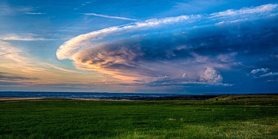 A landscape photo with dark green grass in the foreground and an interesting cloud formation in the sky.