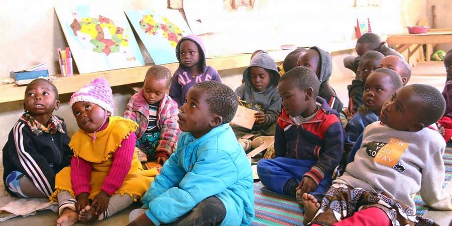 Young students sit on the ground paying attention to a lesson