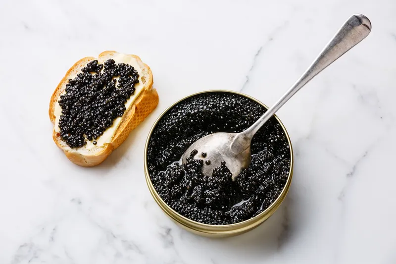 Sturgeon black caviar in can and slice of toast on white marble background