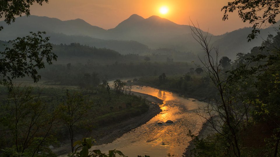 A lush landscape in Nepal with mountains in the background and a winding river at sunrise