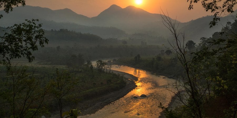 A lush landscape in Nepal with mountains in the background and a winding river at sunrise