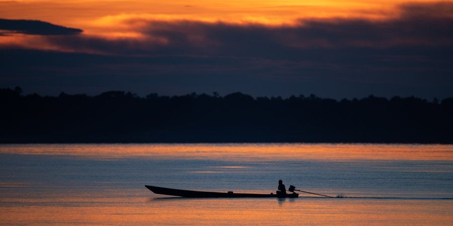 Sunset over body of water with fishing boat in silhouette