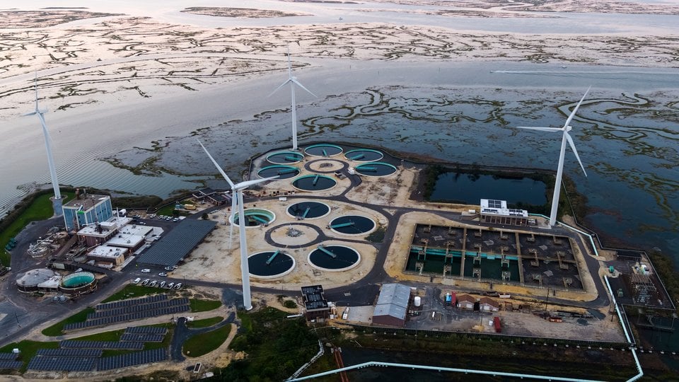 Aerial view at sunset of a wastewater treatment plant powered by wind turbines and solar panels