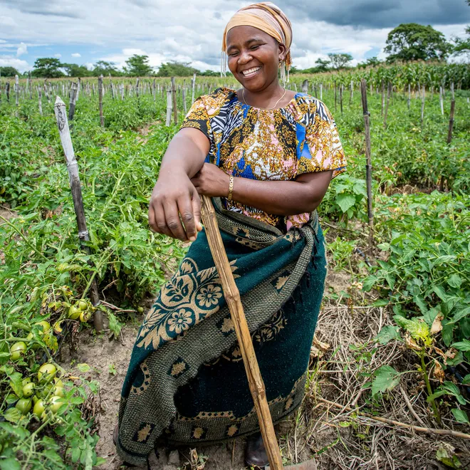 Woman smiles and leans on hoe in field