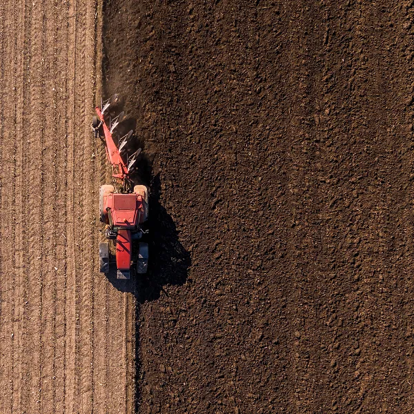 An aerial view of a red tractor moving across overturned soil.