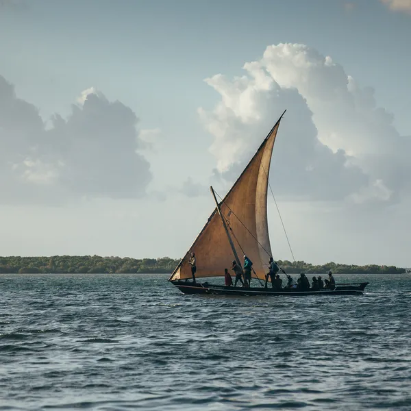 In the evening, a fishing boat with a single triangle sail sets out on the water