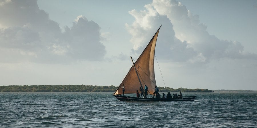In the evening, a fishing boat with a single triangle sail sets out on the water