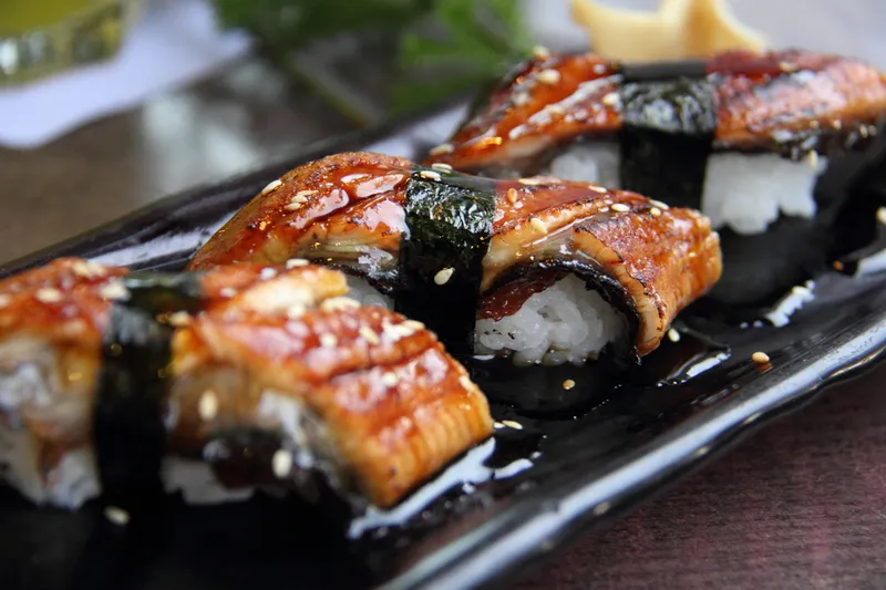 Three pieces of unagi sushi on a black platter