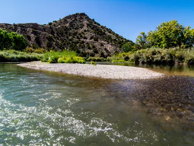 A sunny day over a bend in the Rio Grande River with trees and a rocky beach