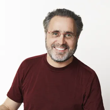 A man wearing a red t-shirt and red rimmed glasses smiles.