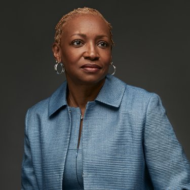 A head shot of a woman wearing hoop earrings and a pale blue suit.