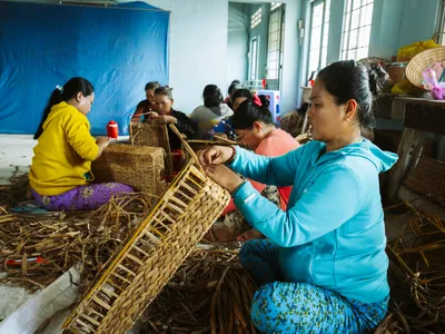 Women weave baskets inside a large room