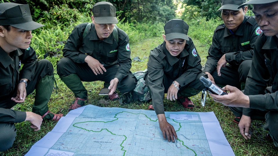 Rangers crouch over map in wooded area