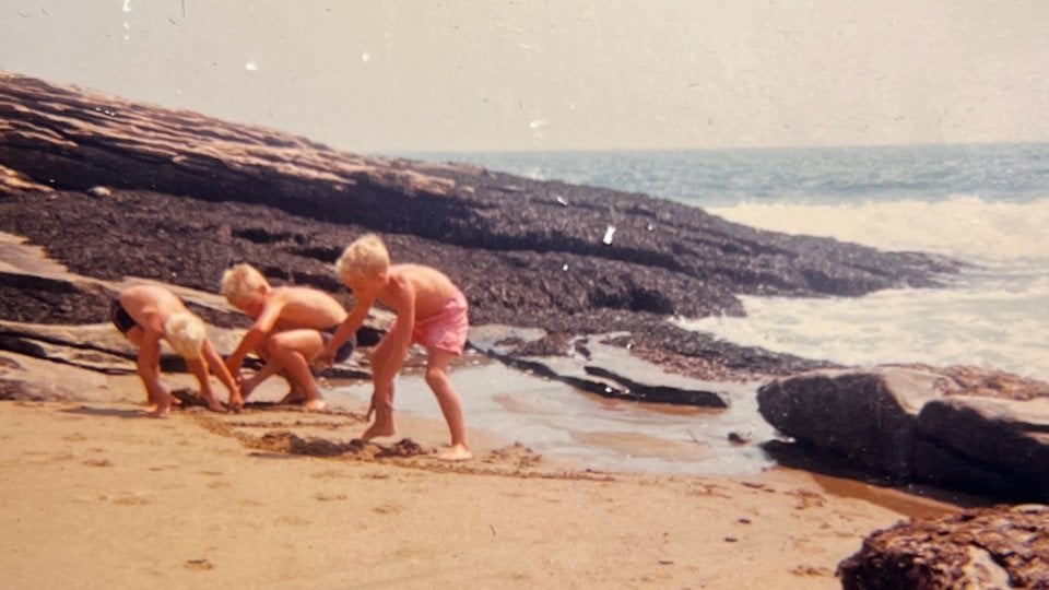 Three blonde boys digging in sand on beach on sunny day