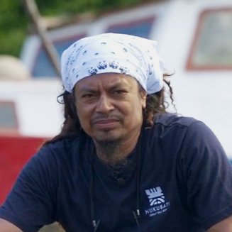 A portrait of Leone Vokai wearing a WWF bandana with a boat visible in the background.