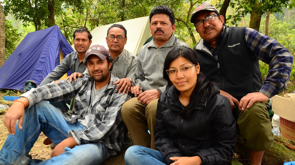 A groupd of people sit together in a forest and smile looking at the camera