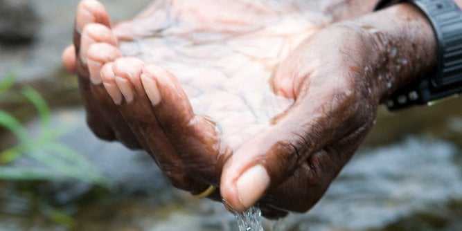 Close-up of cupped hands holding water over a stream