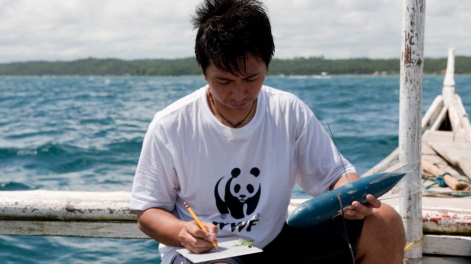 A man sits on a boat and records data from equipment