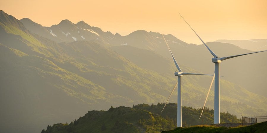 Two wind turbines on a mountain in Alaska with a setting sun and mountains in the background