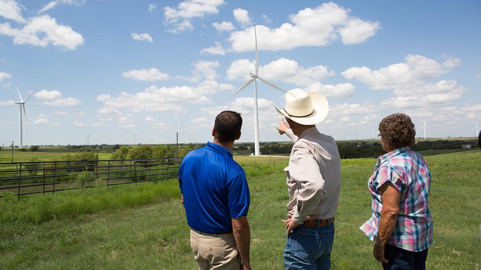 People talking in a field while pointing to a wind turbine