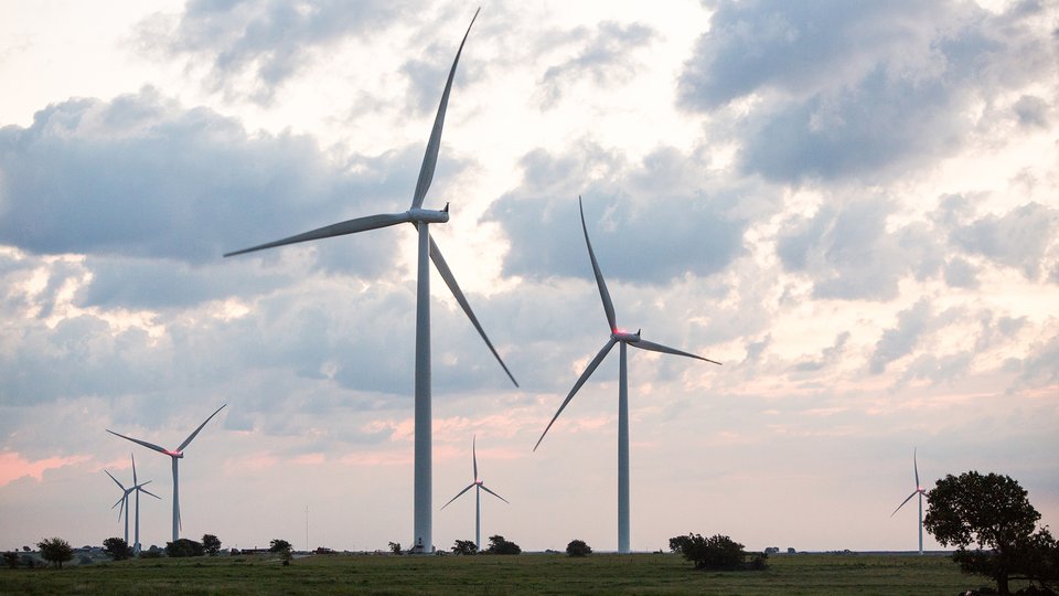 A color photo of a landscape with wind turbines in the center and a cloudy sky in the background