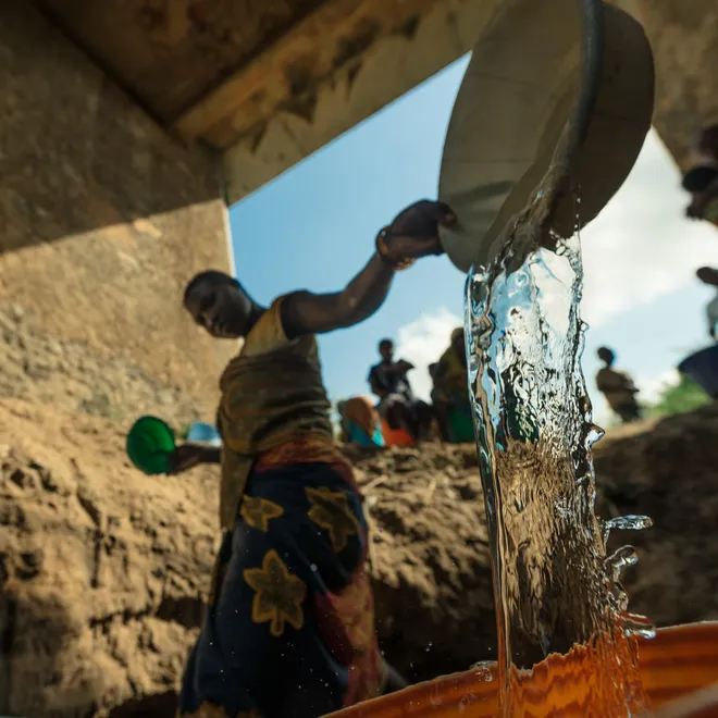 A woman filling up a bucket of water at a makeshift well under a bridge