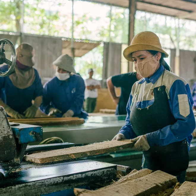 A woman in a mask and gloves feeds a board into a machine