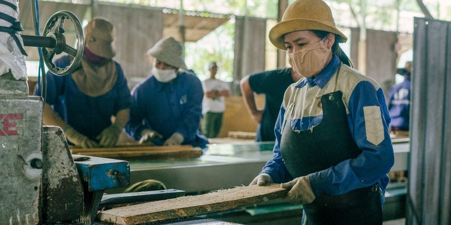 A woman in a mask and gloves feeds a board into a machine