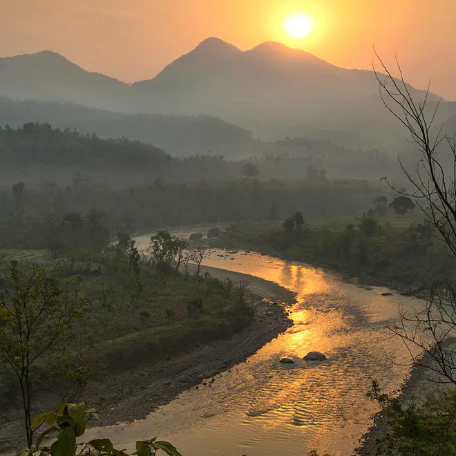 A sunset reflects over a river with mountains silhouetted in the distance