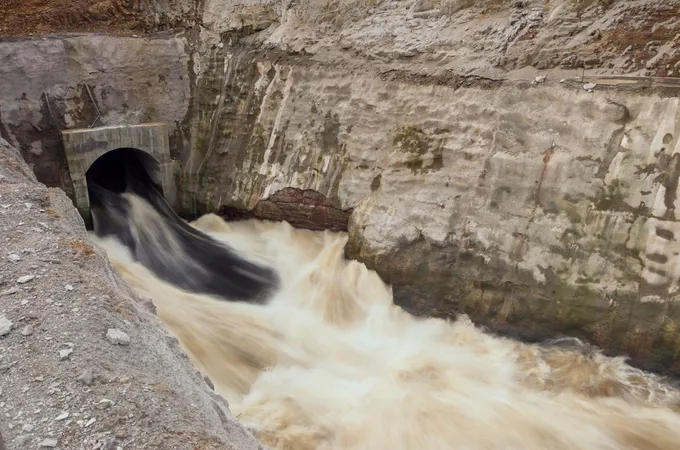 Water rushes through a tunnel in a hydropower dam with brown rock nearby