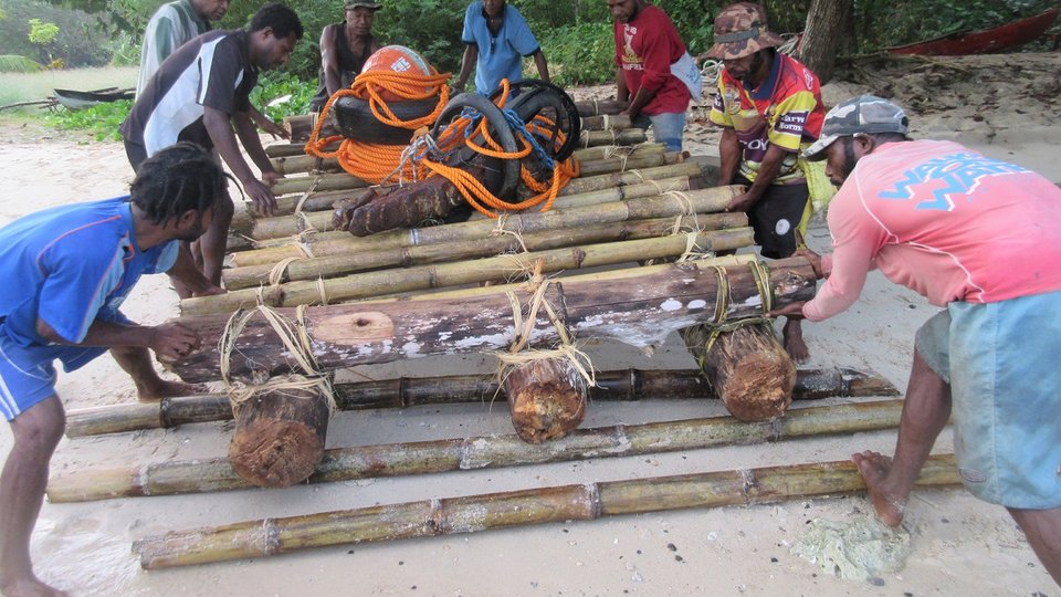 a group of men build a raft on the sand out of wood, bamboo, and rope