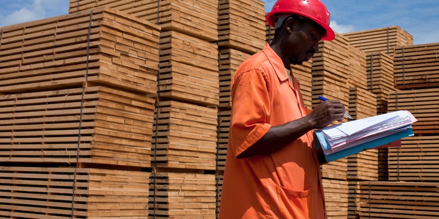 A man checks paperwork in front of stacks of lumber