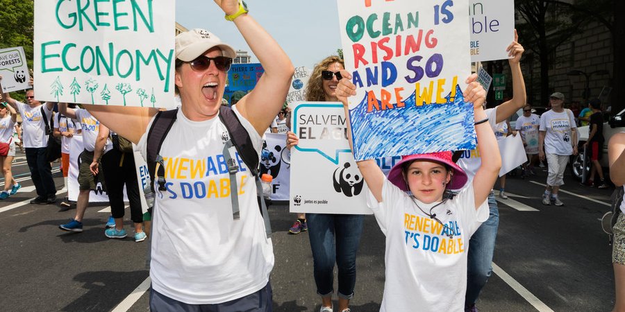people hold up signs that read "green economy" and "the ocean is rising and so are we"