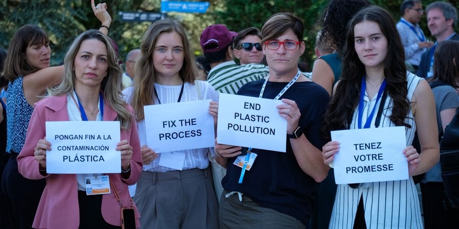 Four women hold signs that demand the end of plastic pollution and a fix to the process during the INC global plastic treaty talks.