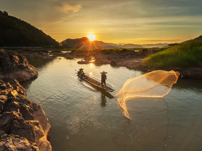 Two fishermen cast nets at sunrise along the Mekong River
