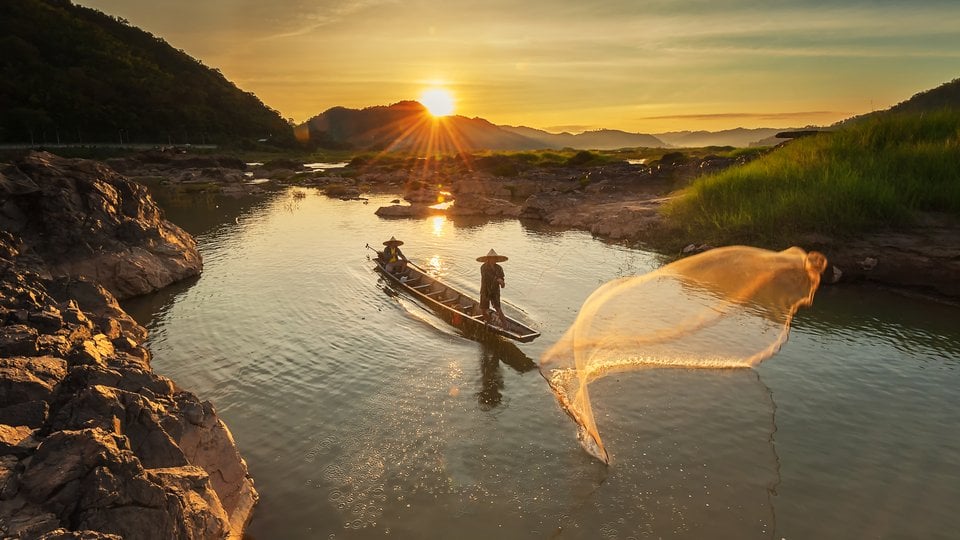 Two fishermen cast nets at sunrise along the Mekong River