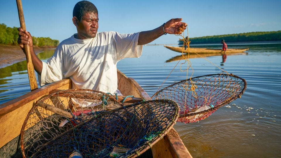 A fisher raises his net out of the water, containing a plastic bottle